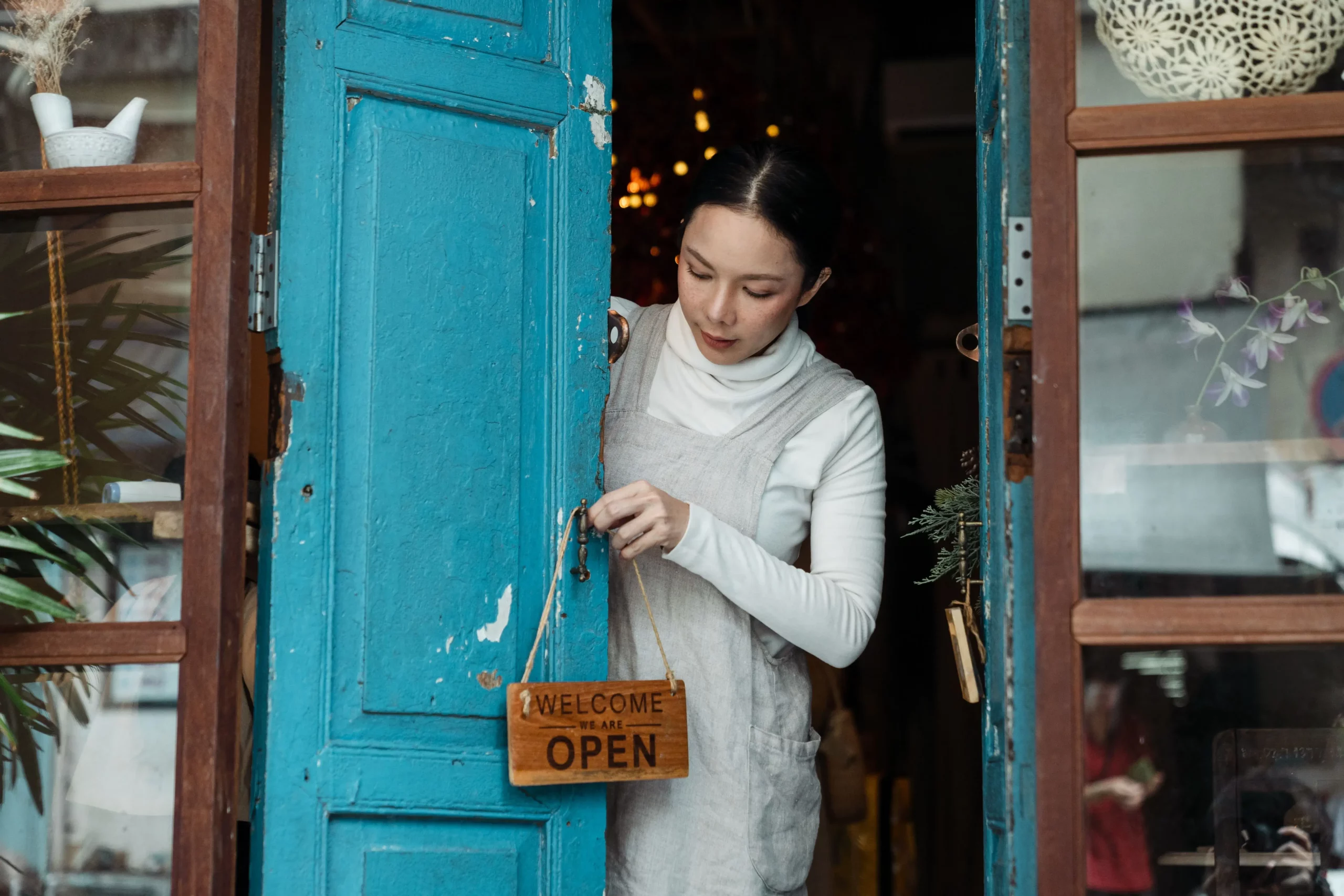 A woman turning the we are open sign at the door of her small independent shop
