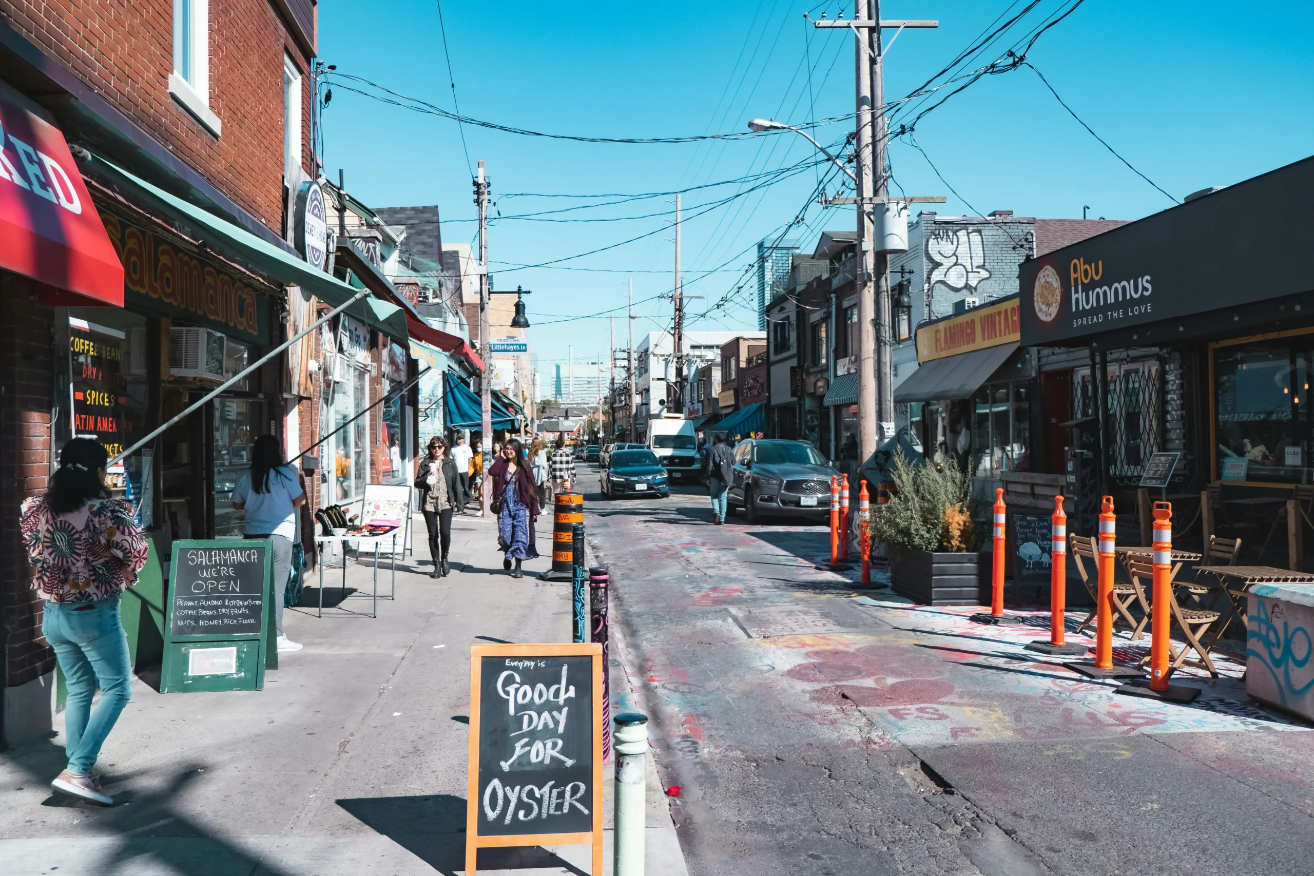 Independent shops and cafés lining a busy city street, with hand-written chalkboard signs on the pavement and people walking past